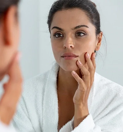 Woman in robe looking in mirror touching face
